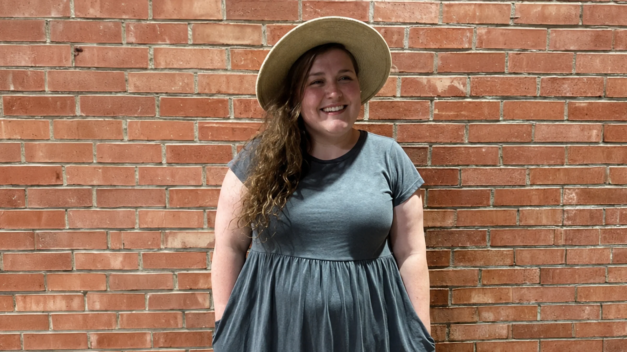 Kaitlynn smiling in a sunhat beside a brick wall