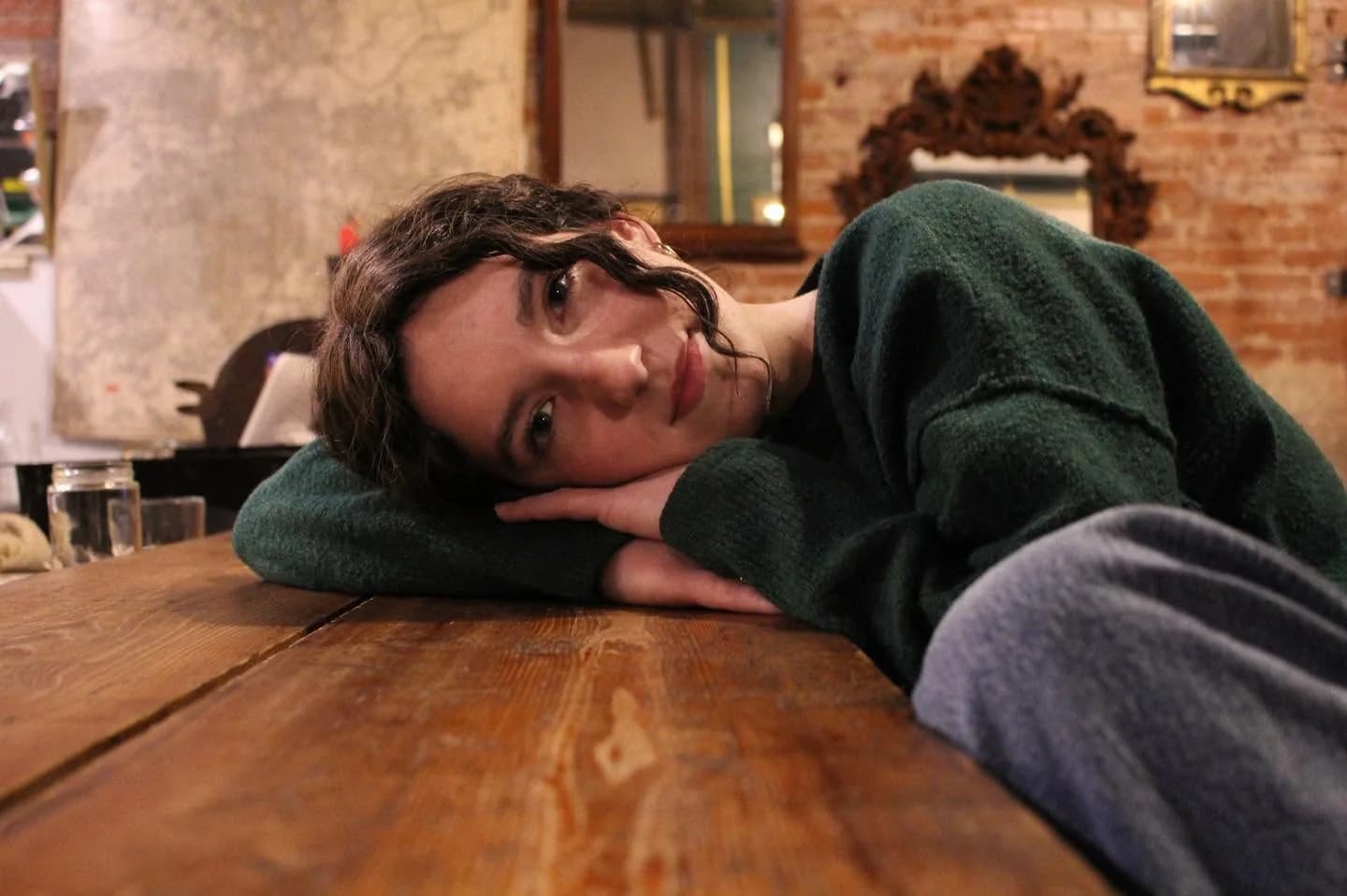 Anna resting her head on her hands at a wooden table